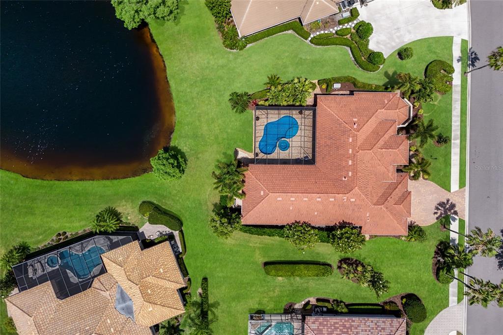 An aerial view shows a house with a tiled roof, pool cage, and surrounding landscaping — 7207 ASHLAND GLEN, LAKEWOOD RANCH, FL
