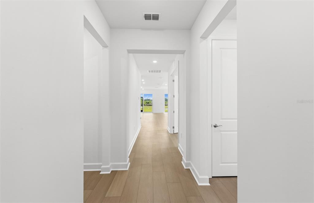A bright hallway with light wood flooring leads toward a distant view of green trees — 16419 LILY ELAINE WAY, BRADENTON, FL