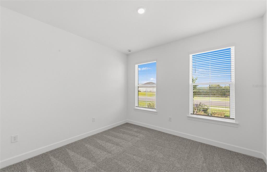 An empty bedroom features white walls, gray carpet, and two windows with white blinds — 16419 LILY ELAINE WAY, BRADENTON, FL