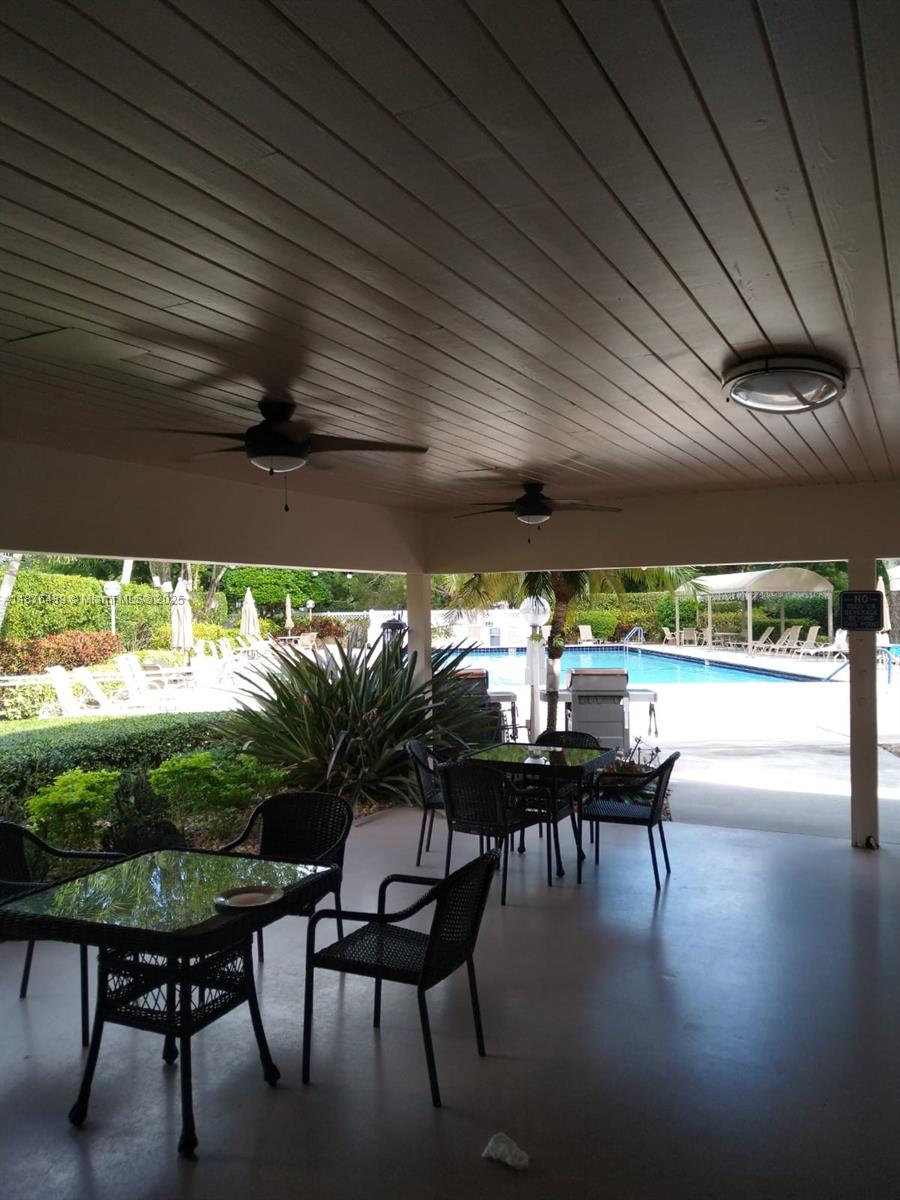 A covered patio features outdoor dining sets, ceiling fans, and a view of a swimming pool — 3510 Oaks Way # 509, Pompano Beach FL 33069, POMPANO BEACH, FL