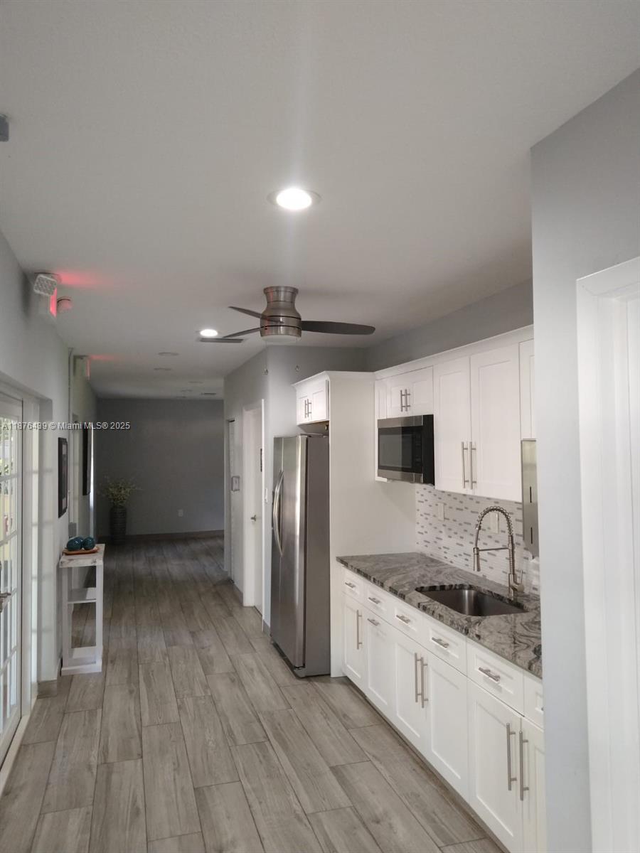 A galley-style kitchen features white cabinets, granite countertops, stainless steel appliances, and wood-look tile flooring — 3510 Oaks Way # 509, Pompano Beach FL 33069, POMPANO BEACH, FL