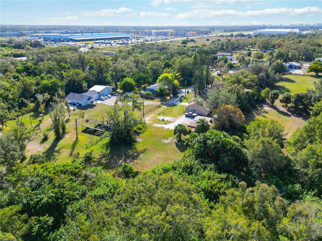An aerial view shows two houses surrounded by trees and a large industrial warehouse nearby — 7560 19TH STREET E, SARASOTA, FL