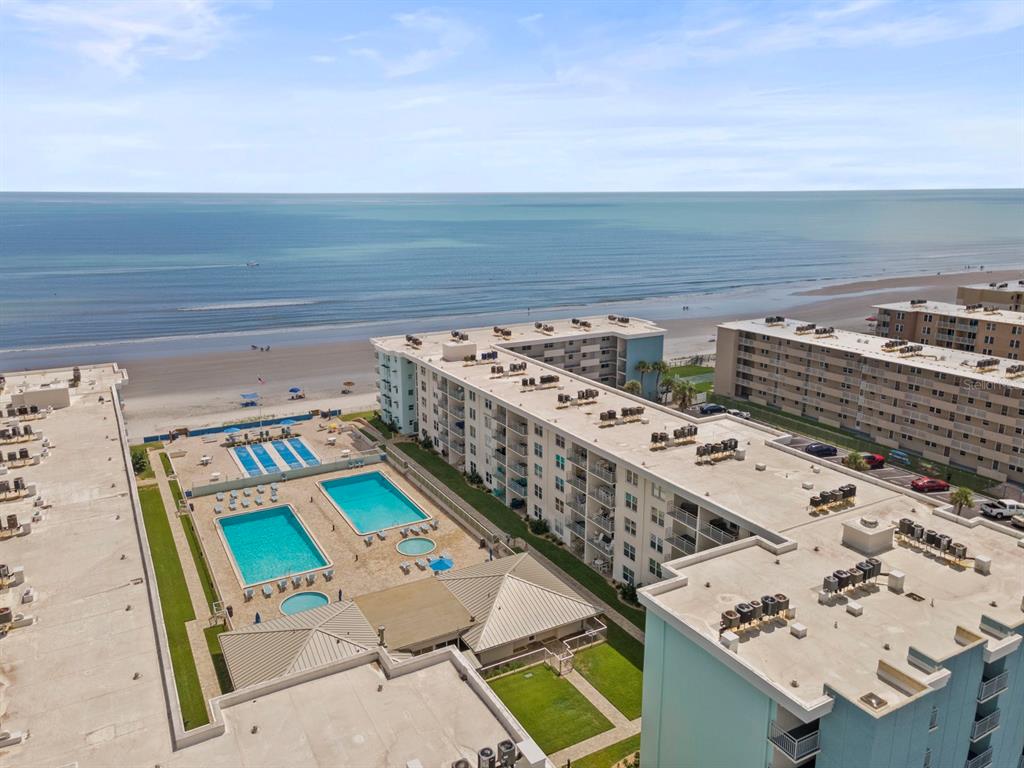 An aerial view shows two multi-story apartment buildings flanking a parking lot near the beach — 4153 S ATLANTIC AVENUE UNIT 5110, NEW SMYRNA BEACH, FL