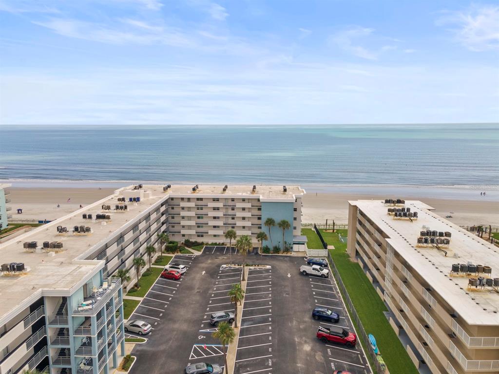 An aerial view of a multi-story beachfront condominium complex with an adjacent parking lot — 4153 S ATLANTIC AVENUE UNIT 5110, NEW SMYRNA BEACH, FL