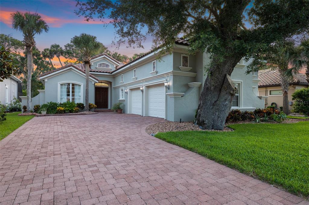 A light-colored two-story house with a brick driveway and a large oak tree in front — 34 S RIVERWALK DRIVE, PALM COAST, FL