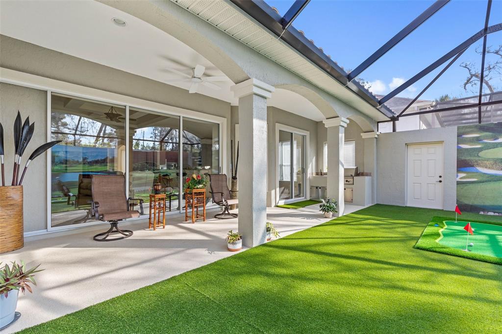 A covered patio features a putting green, outdoor kitchen, and sliding glass doors to the home — 34 S RIVERWALK DRIVE, PALM COAST, FL