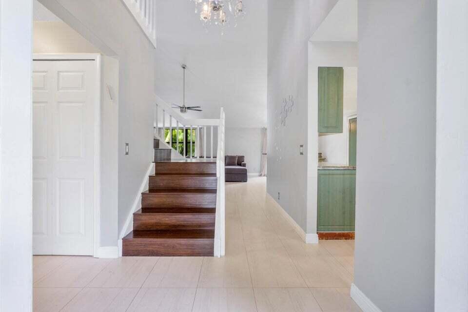 A foyer features light tile flooring, a wooden staircase, and a view into a living area — 4140 Woods End Road, Boca Raton FL 33487, BOCA RATON, FL
