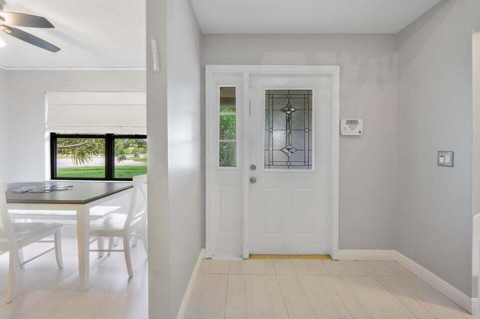 A bright entryway features a white front door with a sidelight and light tile flooring — 4140 Woods End Road, Boca Raton FL 33487, BOCA RATON, FL