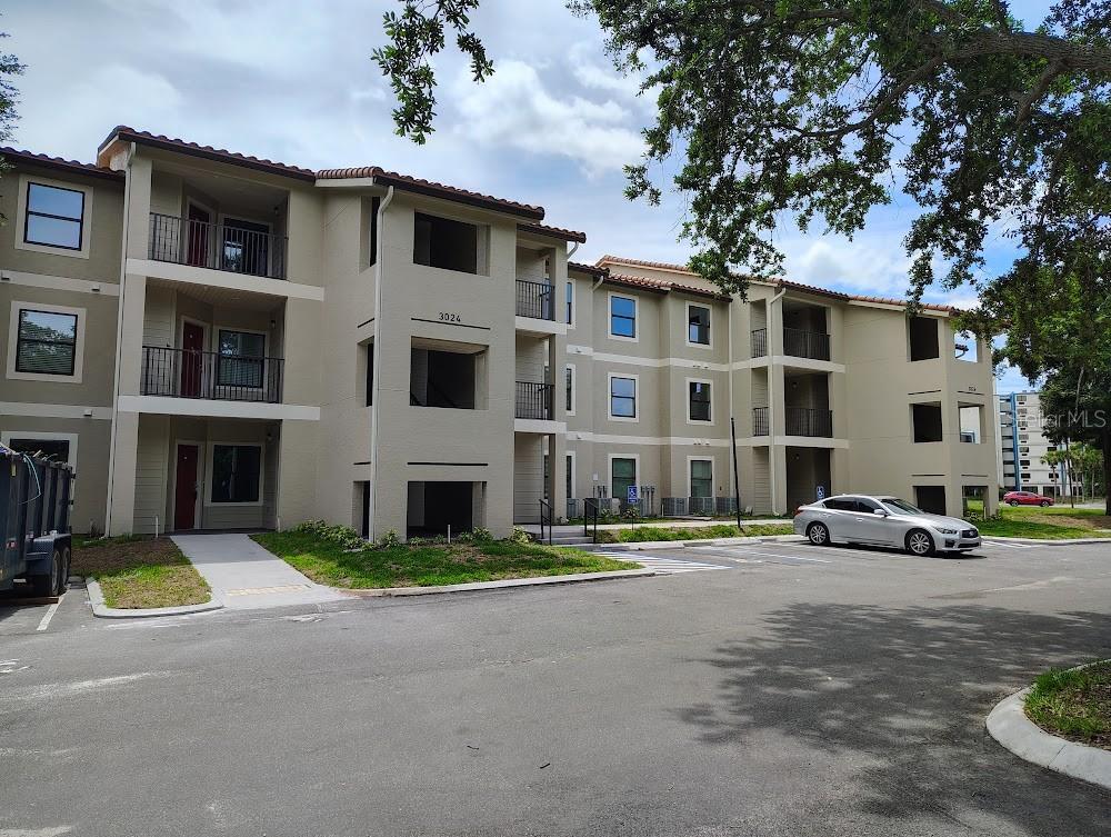 A multi-story apartment building with beige stucco walls, balconies, and a parking lot in front — 3024 PARKWAY BOULEVARD UNIT 202, KISSIMMEE, FL