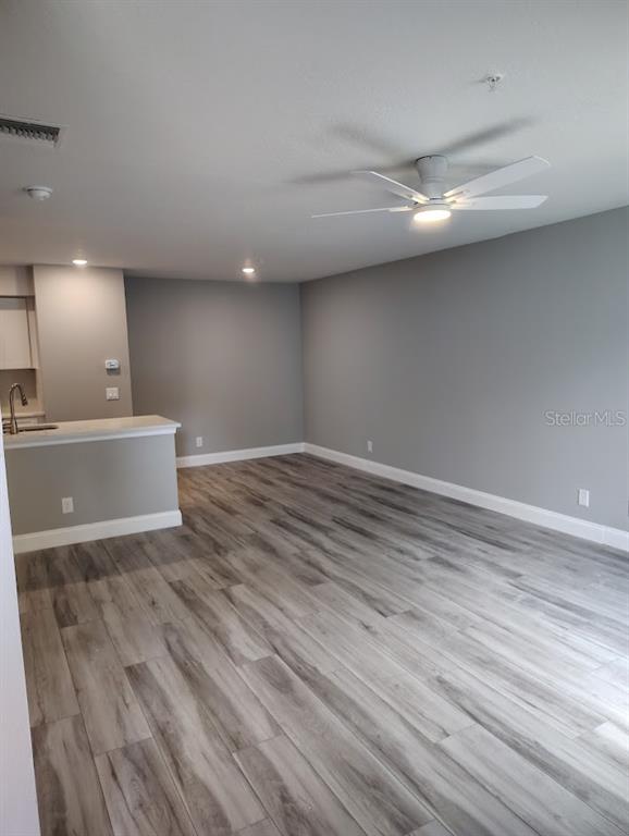 An empty living area features gray walls, wood-look flooring, and a white ceiling fan — 3024 PARKWAY BOULEVARD UNIT 202, KISSIMMEE, FL
