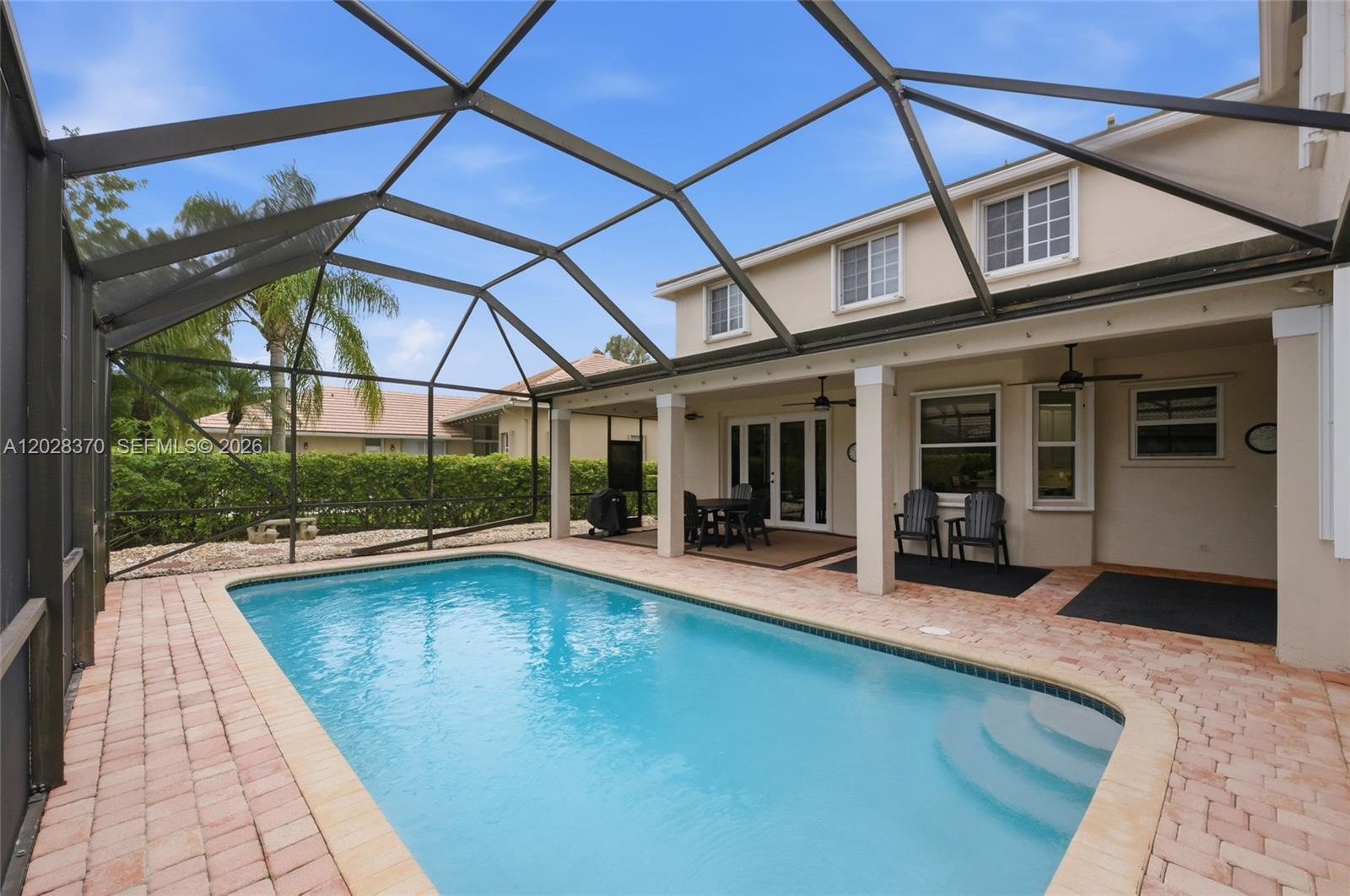 A swimming pool sits on a brick patio inside a screened-in outdoor enclosure — 2608 Oakbrook Ct, Weston FL 33332, WESTON, FL