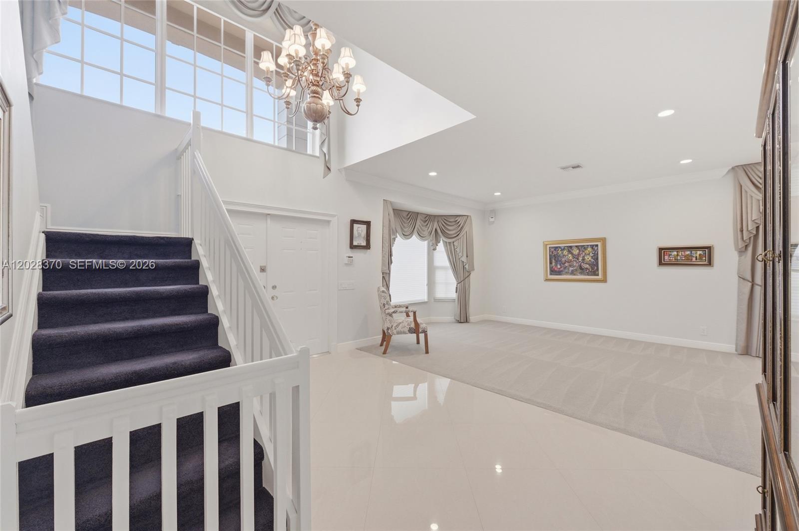 A bright foyer features a dark-carpeted staircase, a crystal chandelier, and a spacious living area — 2608 Oakbrook Ct, Weston FL 33332, WESTON, FL
