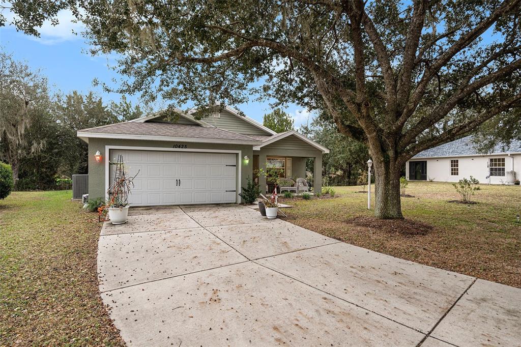 A single-story house with a two-car garage and a large oak tree in the yard — 10425 S DREW BRYANT CIRCLE, FLORAL CITY, FL