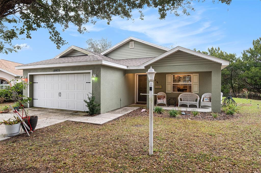 A single-story house with a green stucco exterior, a two-car garage, and a front porch — 10425 S DREW BRYANT CIRCLE, FLORAL CITY, FL