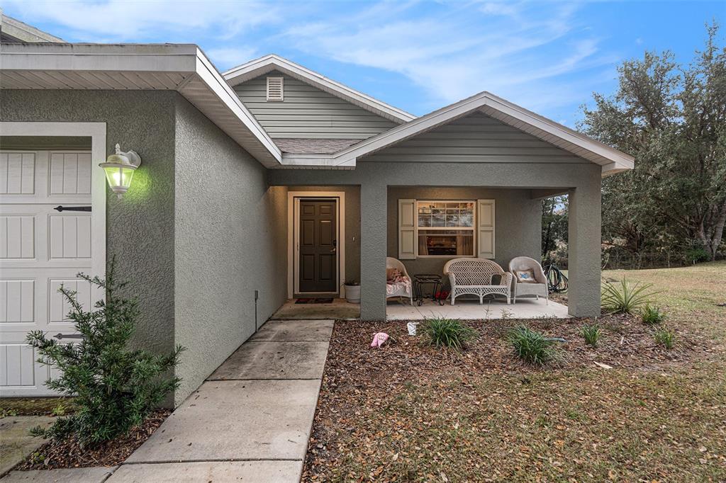 A single-story house exterior features a covered front porch, a garage, and a concrete walkway — 10425 S DREW BRYANT CIRCLE, FLORAL CITY, FL
