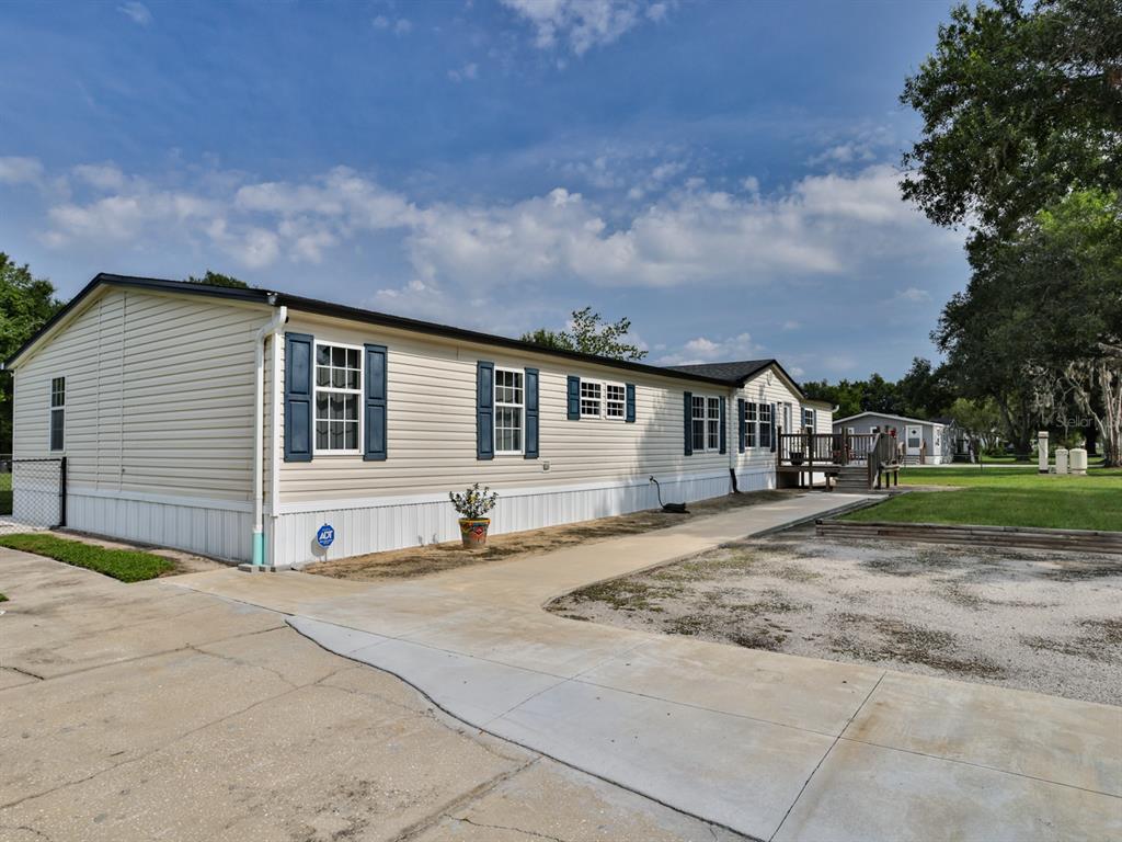 A beige manufactured home with blue shutters sits on a concrete lot with a deck — 1120 SADDLEWOOD BOULEVARD, LAKELAND, FL