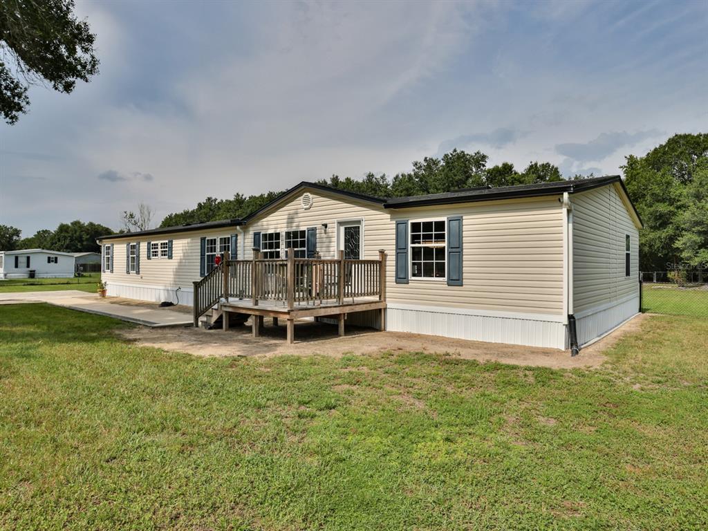 A tan manufactured home features a wooden deck, blue shutters, and a concrete patio area — 1120 SADDLEWOOD BOULEVARD, LAKELAND, FL