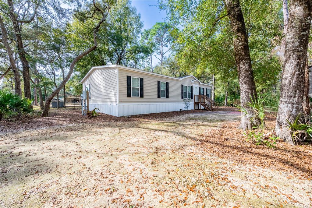 A light-colored mobile home sits at the end of a gravel driveway behind a gate — 11120 NW 107TH TERRACE, CHIEFLAND, FL