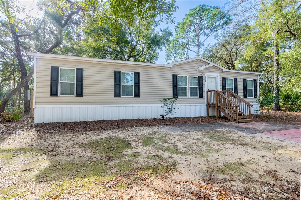 A single-story manufactured home with beige siding sits in a wooded, sandy lot — 11120 NW 107TH TERRACE, CHIEFLAND, FL