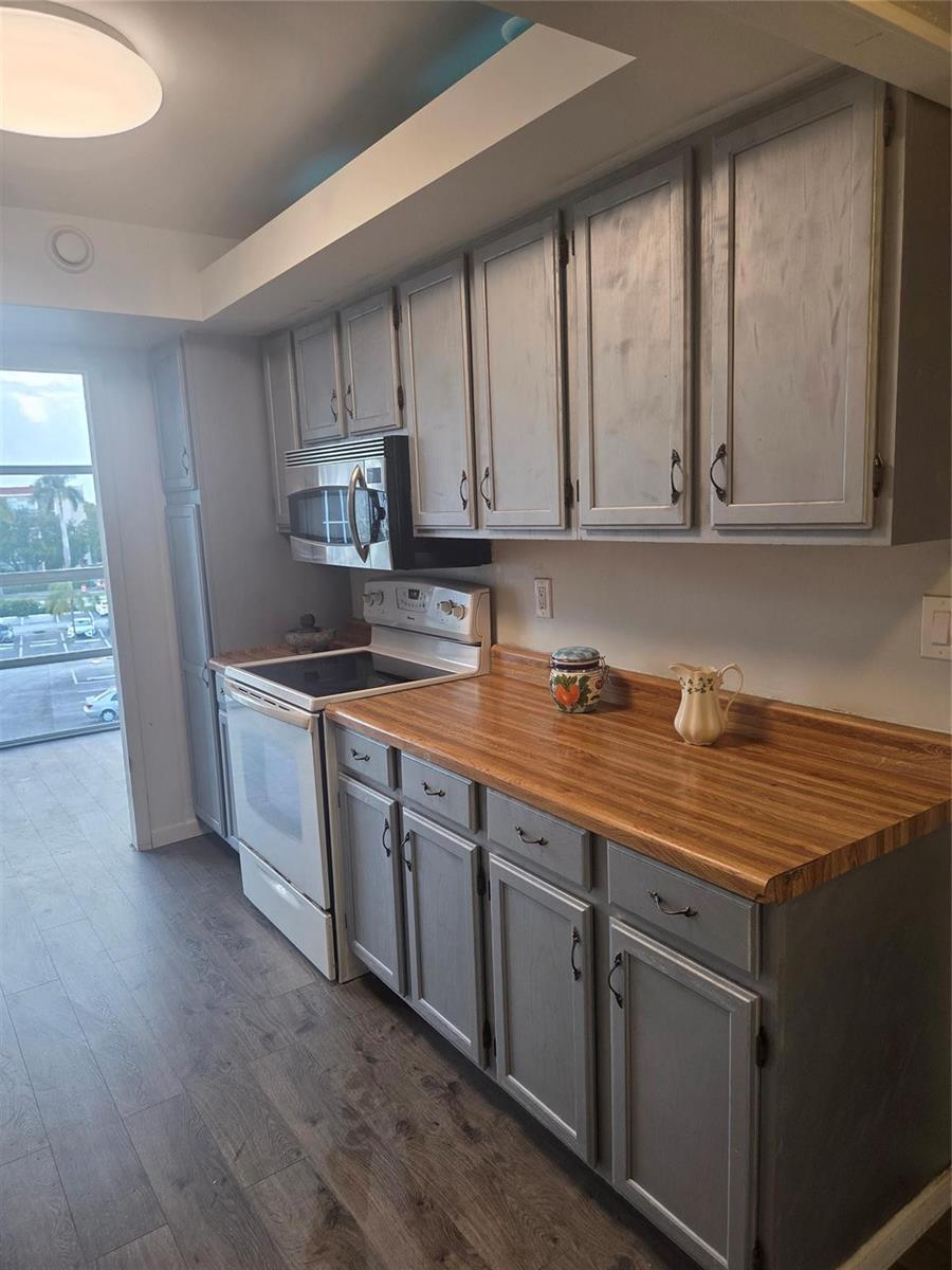 A kitchen features gray painted cabinets, a wood-look laminate countertop, and a white electric range — 801 Three Islands Boulevard # 409, Hallandale Beach FL 33009, HALLANDALE BEACH, FL