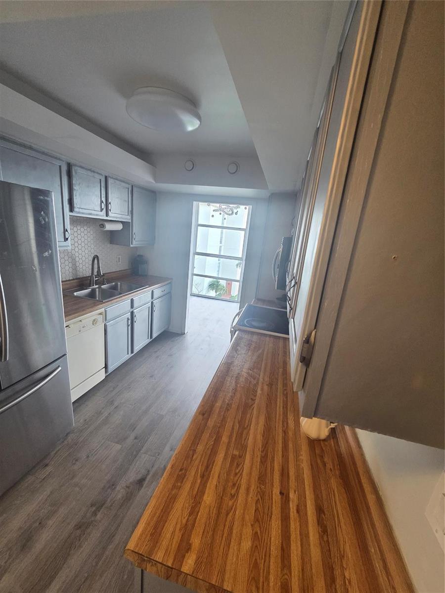 A galley kitchen features gray cabinets, wood-look countertops, stainless steel appliances, and a windowed door — 801 Three Islands Boulevard # 409, Hallandale Beach FL 33009, HALLANDALE BEACH, FL