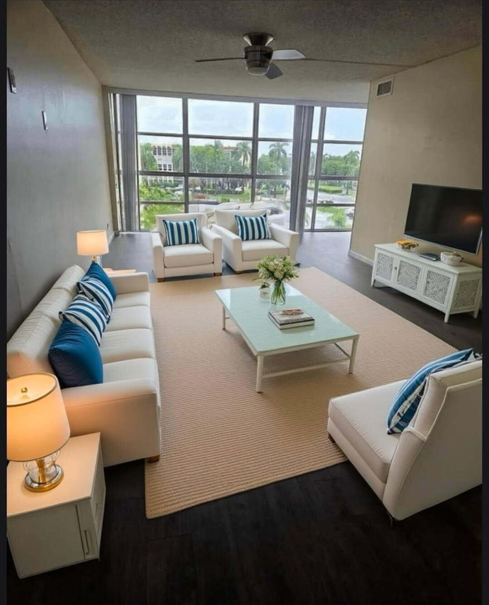 A bright living room features white furniture, blue striped pillows, a glass table, and floor-to-ceiling windows — 801 Three Islands Boulevard # 409, Hallandale Beach FL 33009, HALLANDALE BEACH, FL