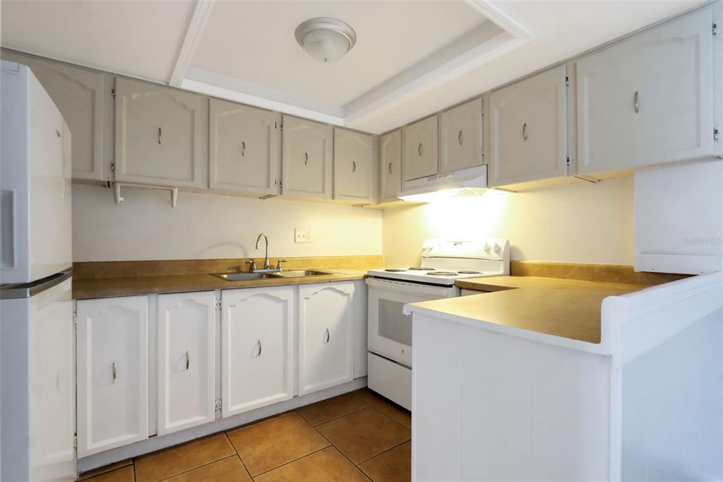 A kitchen with white cabinets, tan countertops, a white stove, and brown tile flooring — 1902 HONOUR ROAD UNIT 11, ORLANDO, FL