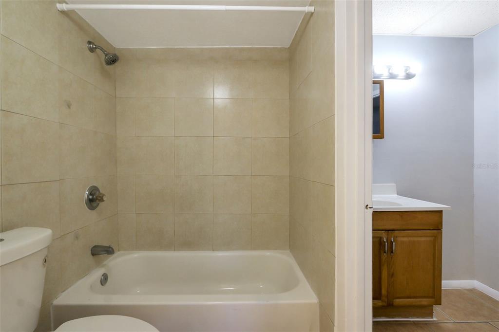 A bathroom features a tiled shower-tub combination next to a vanity with a wooden cabinet — 1902 HONOUR ROAD UNIT 11, ORLANDO, FL