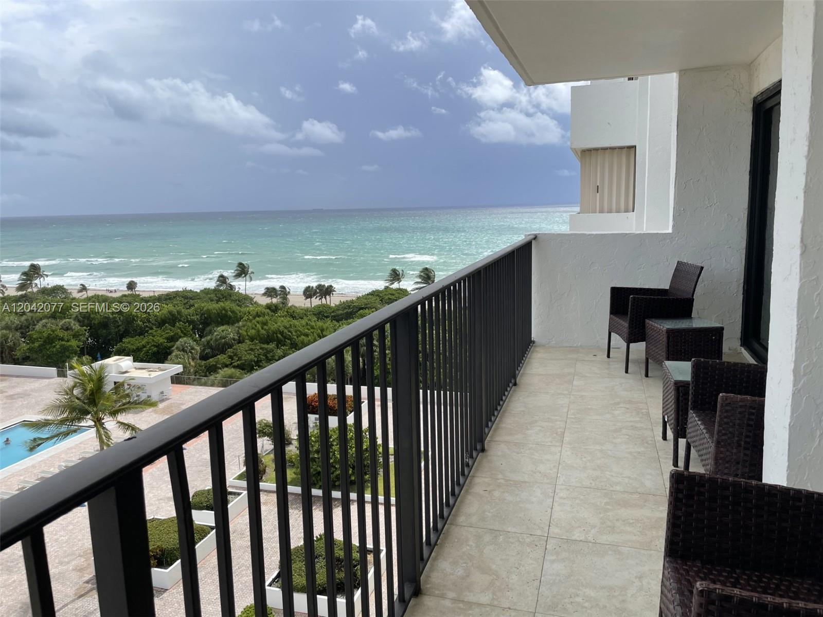 A balcony with dark metal railings overlooks a swimming pool, lush trees, and the ocean — 1201 S Ocean Dr # 1107S, Hollywood FL 33019, HOLLYWOOD, FL