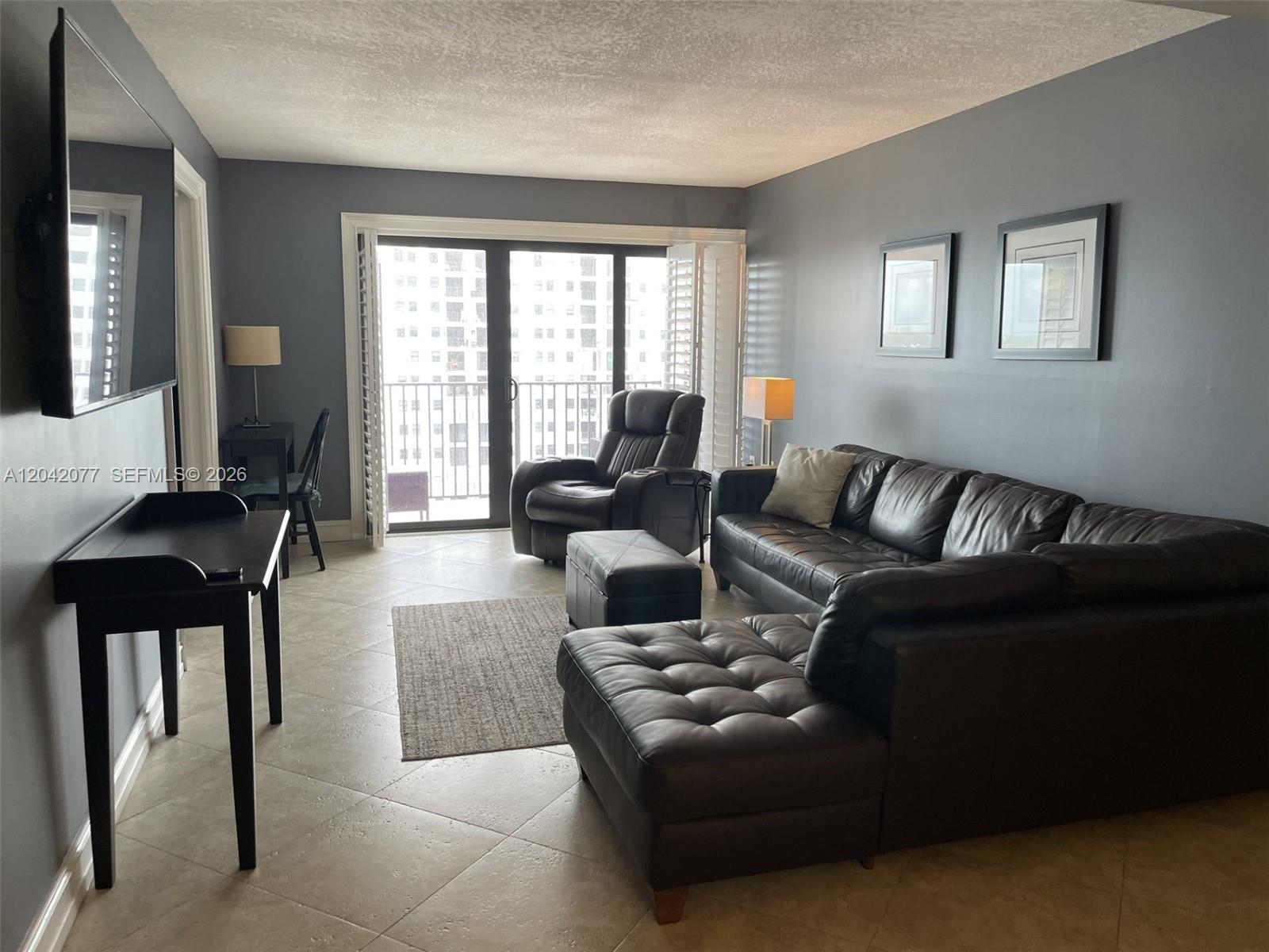 A living room features dark gray walls, tile flooring, a leather sectional, and a balcony — 1201 S Ocean Dr # 1107S, Hollywood FL 33019, HOLLYWOOD, FL