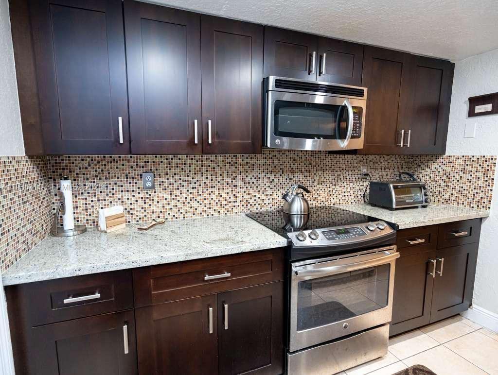 A kitchen features dark wood cabinets, granite countertops, a tiled backsplash, and stainless steel appliances — 8600 SW 109th Ave # 114, Miami FL 33173, MIAMI, FL