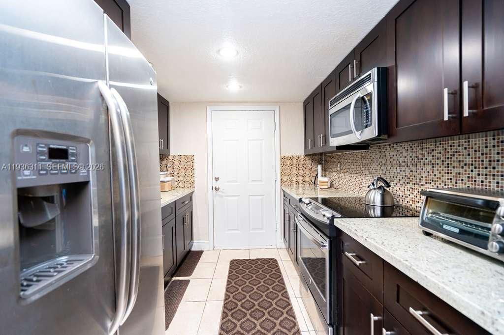 A galley kitchen features dark wood cabinets, granite countertops, stainless steel appliances, and tile flooring — 8600 SW 109th Ave # 114, Miami FL 33173, MIAMI, FL