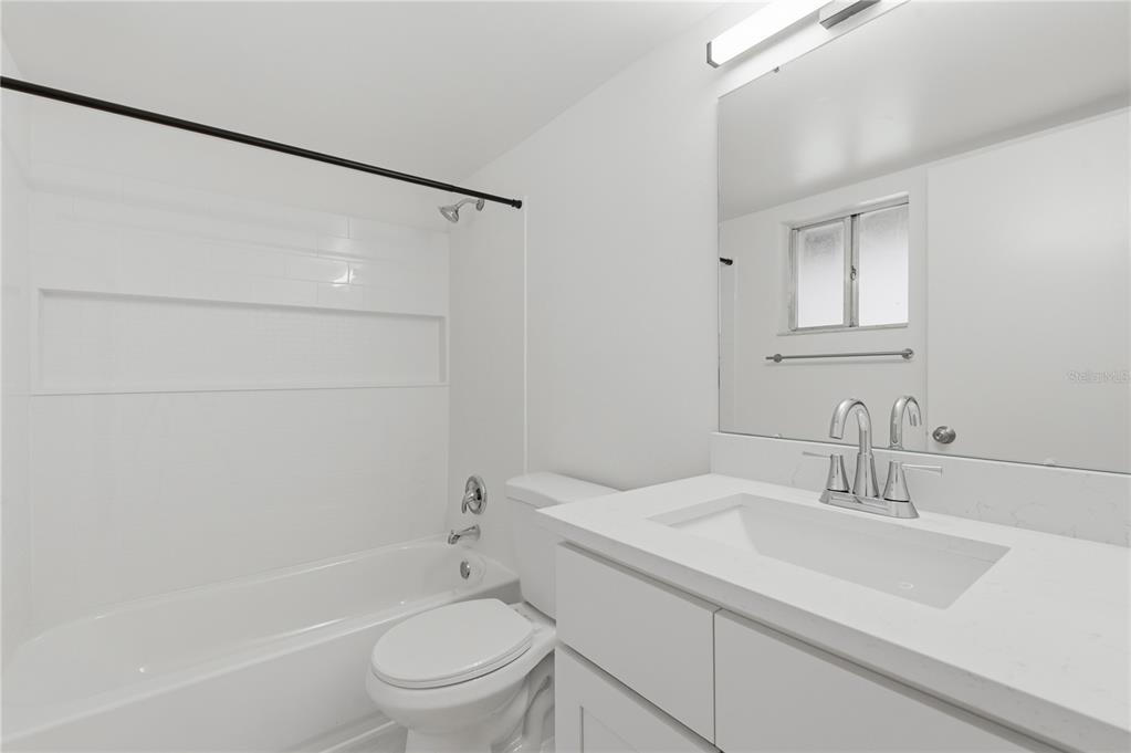 A white bathroom features a vanity with a quartz countertop, a toilet, and a tub-shower — 1100 TURNER STREET, CLEARWATER, FL