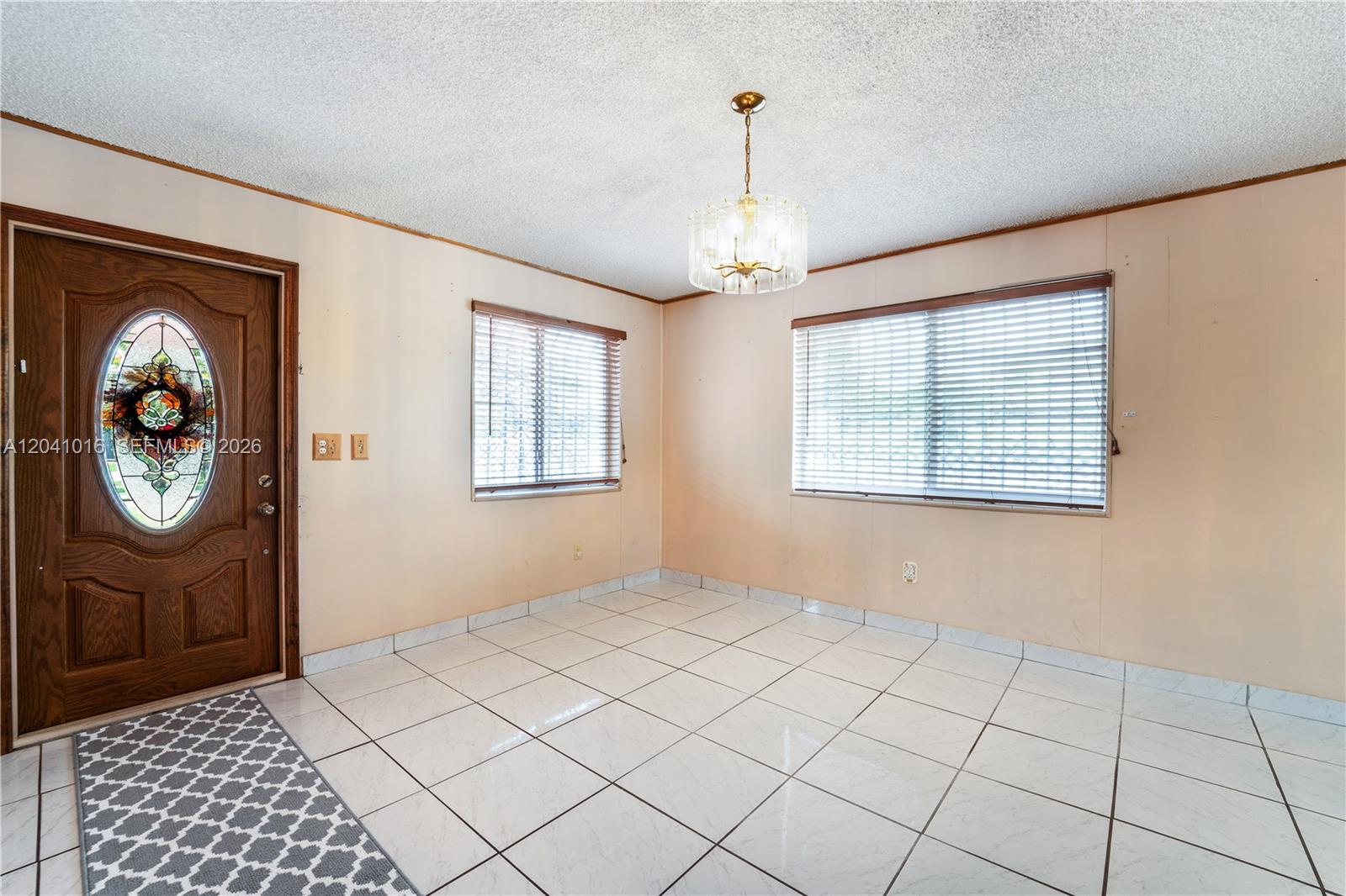 An empty room features white tile flooring, a crystal chandelier, and a stained-glass front door — 11941 SW 4th St, Miami FL 33184, MIAMI, FL