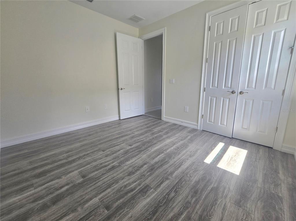 An empty bedroom features light-colored walls, gray wood-look flooring, and white closet doors — 333 VILLORESI BOULEVARD, NOKOMIS, FL