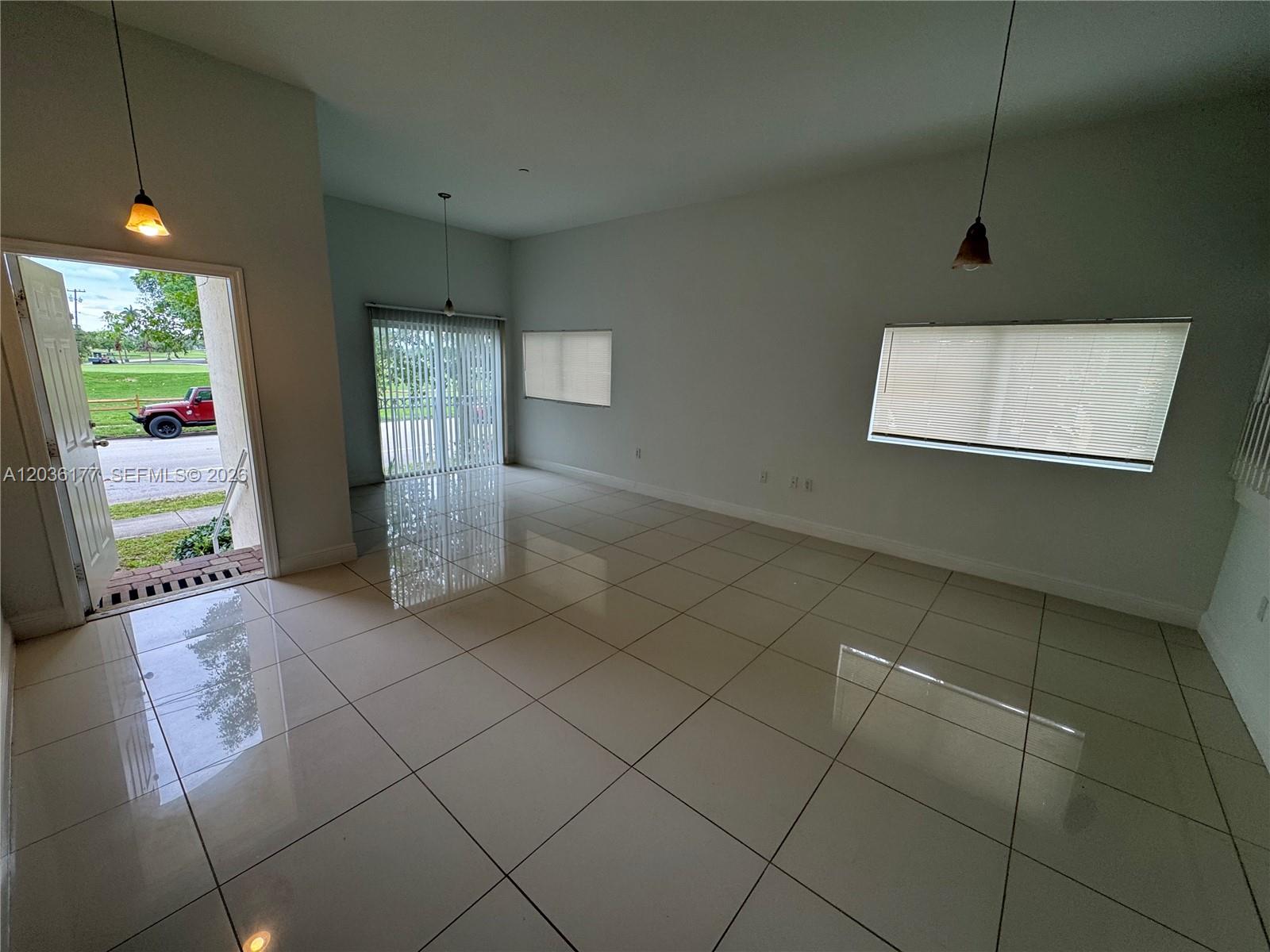An empty room features large white floor tiles, pendant lighting, and a view of a driveway — 820 N 17th Ave, Hollywood FL 33020, HOLLYWOOD, FL