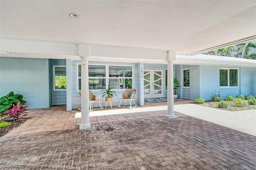 A covered brick entryway leads to a light blue house with white columns and chairs — 4852 FEATHERBED LANE, SARASOTA, FL
