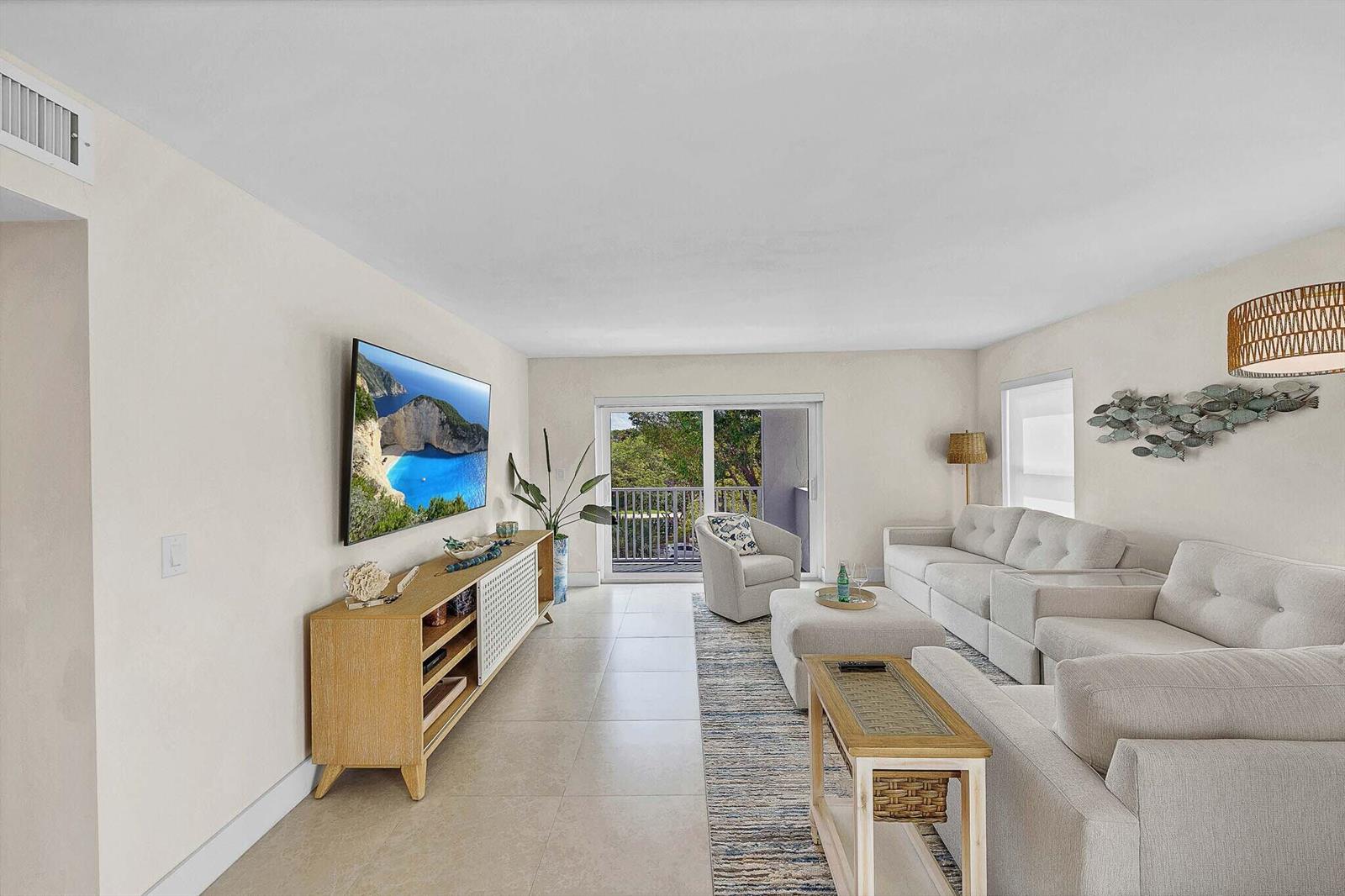 A living room features a wall-mounted television, a light wood media console, and neutral furniture — 1111 S Ocean Boulevard # 414, Boca Raton FL 33432, BOCA RATON, FL