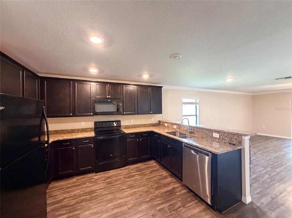 A kitchen features dark wood cabinets, granite countertops, black appliances, and wood-look flooring — 1880 PIEDMONT COURT, MASCOTTE, FL