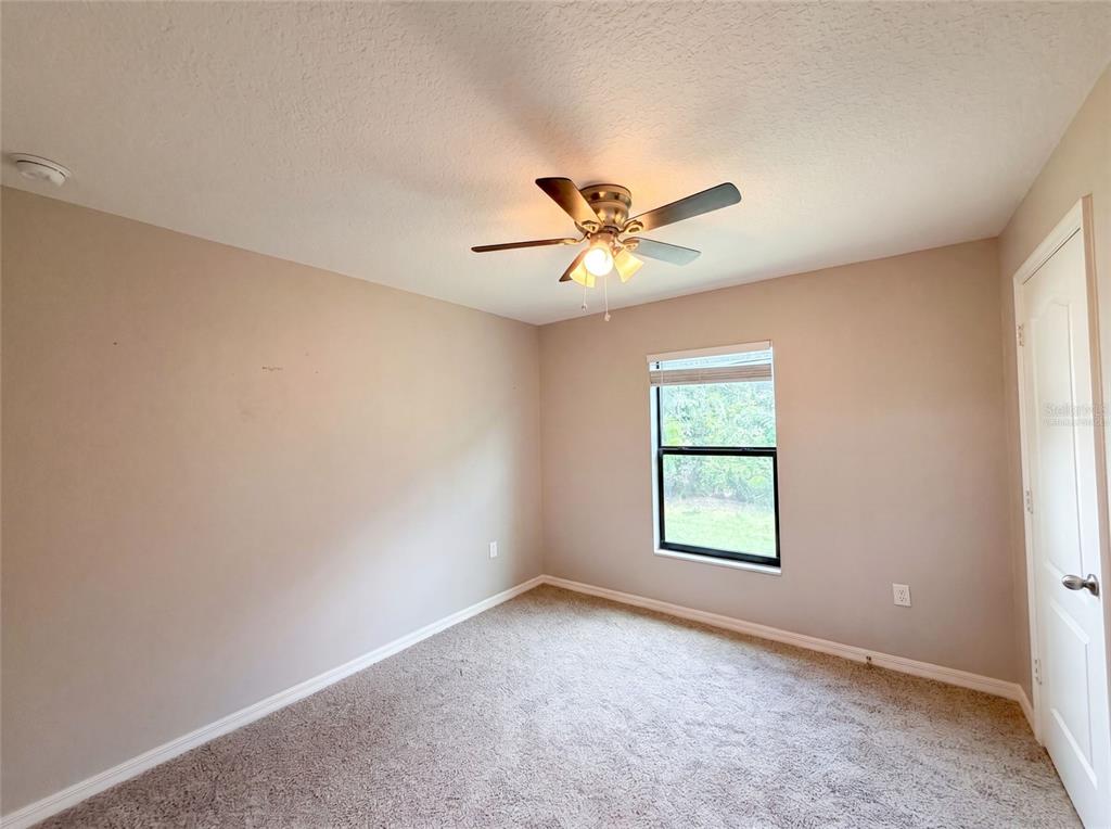 A bedroom with beige walls, tan carpeting, a ceiling fan, and a single window — 1880 PIEDMONT COURT, MASCOTTE, FL