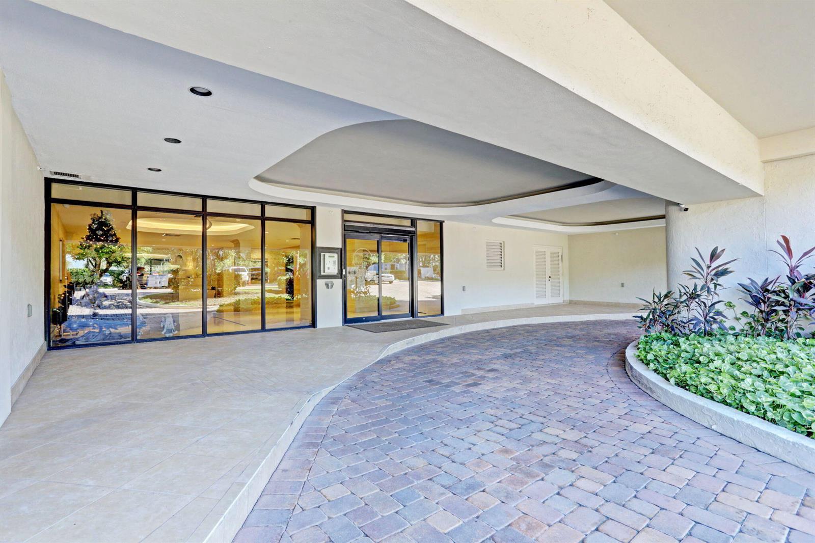A paved driveway leads to the glass-fronted entrance of a building with a covered portico — 3440 S Ocean Boulevard # 105s, Palm Beach FL 33480, PALM BEACH, FL
