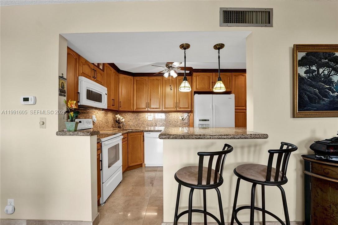 A kitchen with wood cabinets, granite countertops, and a breakfast bar with two stools — 1400 S Ocean Dr # 1004, Hollywood FL 33019, HOLLYWOOD, FL