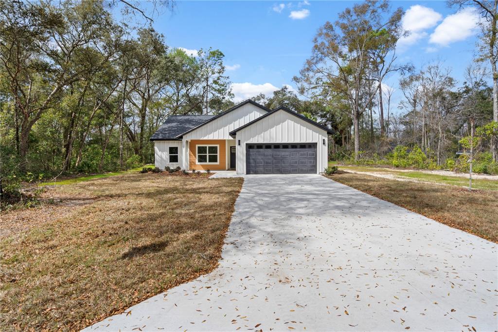 A covered concrete porch features tan siding, a white window, and a view of trees — 11380 NW 92ND CT, CHIEFLAND, FL