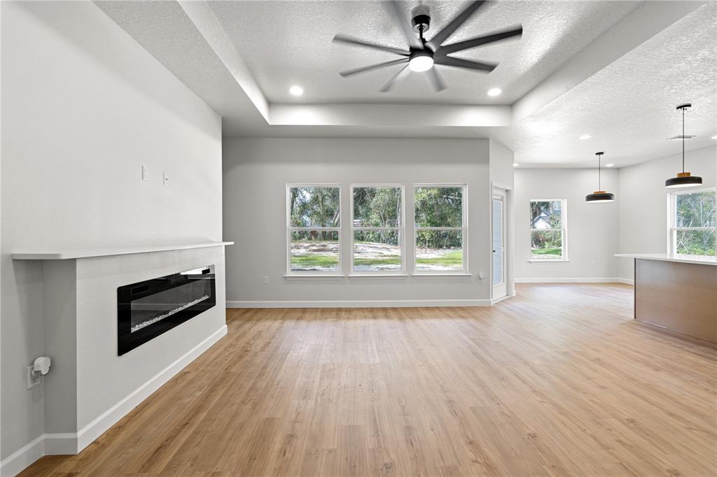 A view from a hallway into a living room with wood-look flooring and three windows — 11380 NW 92ND CT, CHIEFLAND, FL