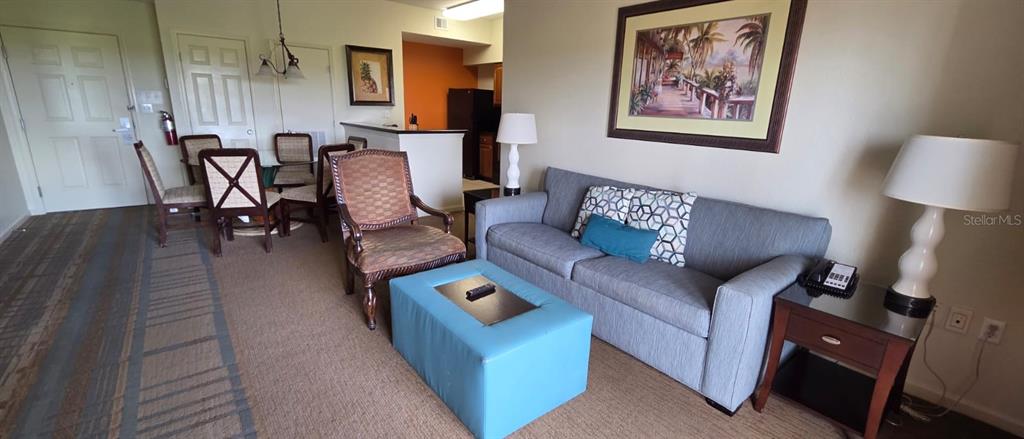 A living room features a gray sofa, a blue ottoman, and a dining area nearby — 8125 RESORT VILLAGE DRIVE UNIT 5803, ORLANDO, FL