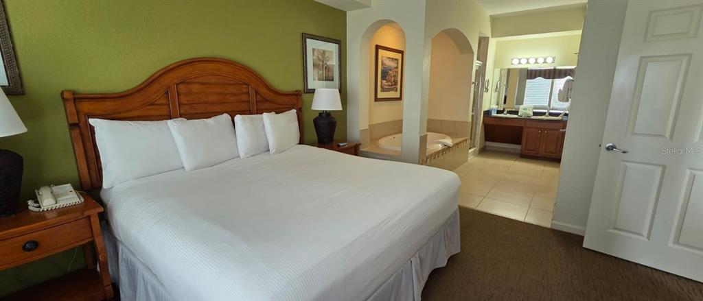 A bedroom features a large bed, a wooden headboard, and an attached bathroom with a tub — 8125 RESORT VILLAGE DRIVE UNIT 5803, ORLANDO, FL