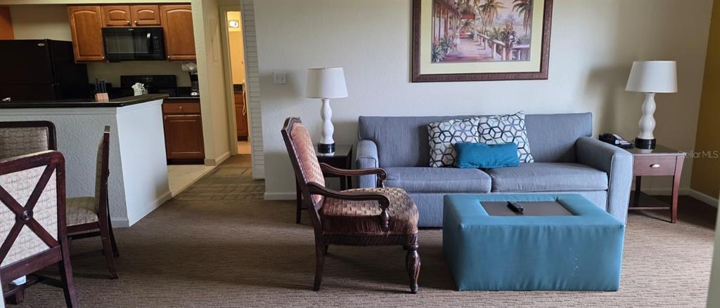 A living room features a gray sofa, a teal ottoman, and an adjacent kitchen area — 8125 RESORT VILLAGE DRIVE UNIT 5803, ORLANDO, FL