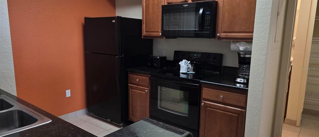 A kitchen features dark wood cabinets, black appliances, and an orange accent wall — 8125 RESORT VILLAGE DRIVE UNIT 5803, ORLANDO, FL