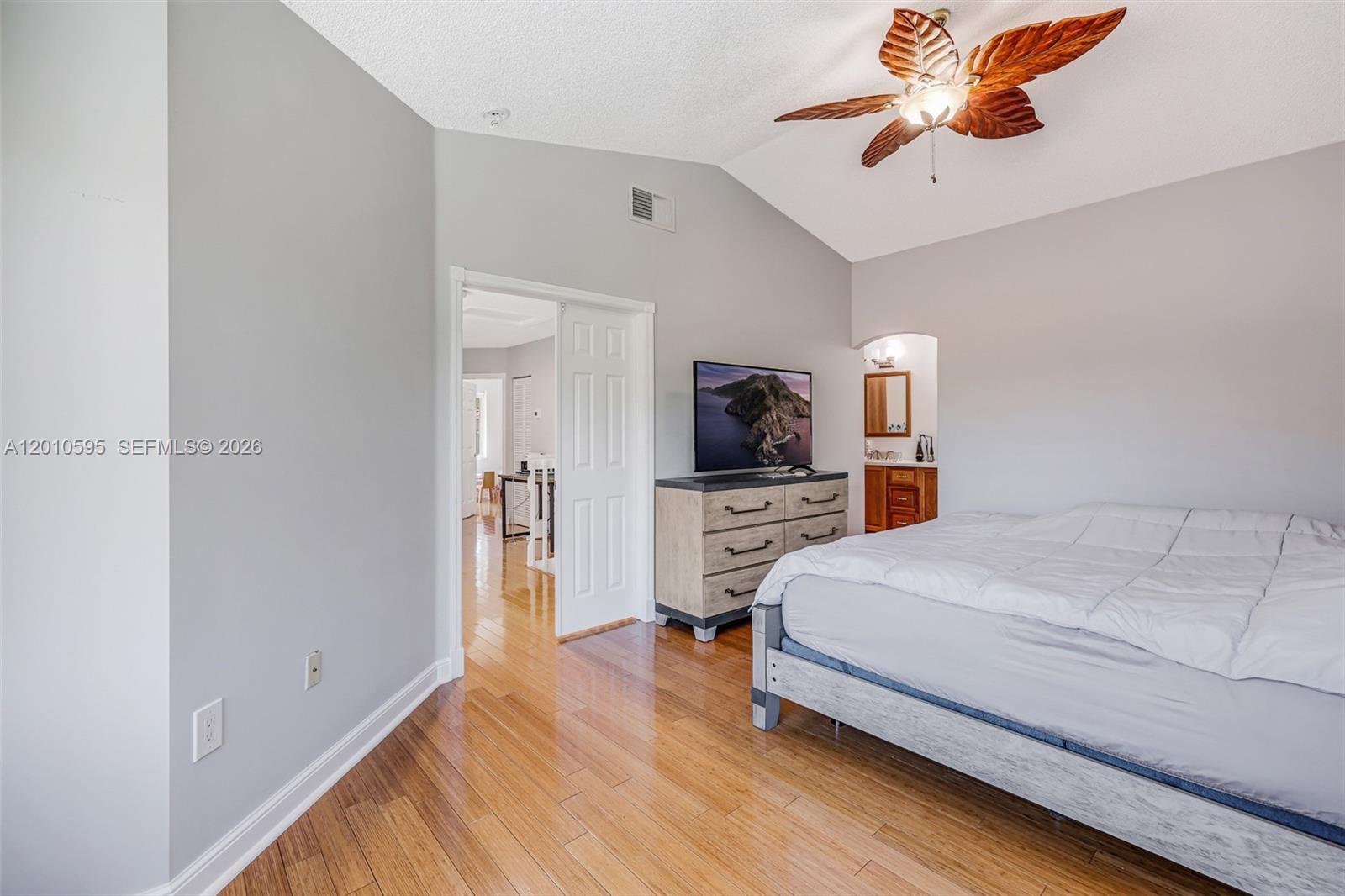 A bedroom features hardwood floors, a vaulted ceiling with a leaf-shaped fan, and a dresser — 1065 Weeping Willow Way, Hollywood FL 33019, HOLLYWOOD, FL