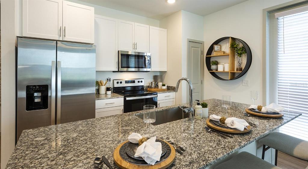 A kitchen features white cabinets, stainless steel appliances, granite countertops, and a central island — 4980 RED MAPLE LANE UNIT C1, WILDWOOD, FL